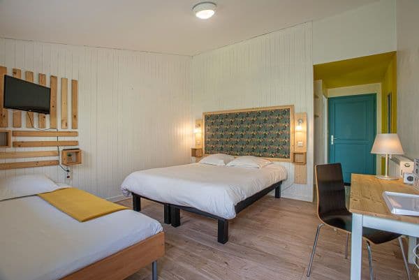 gîte à audierne - chambre familiale avec un lit double et un lit simple. Les murs de la chambres sont blanc, avec des décorations en bois alors que les murs du couloirs menant à la salle de bain sont vert anis avec la porte turquoise