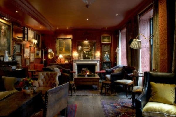 Intérieur du salon de l'hôtel avec une décoration très cosy british avec de gros fauteuil et une cheminée allumée au fond de la piece