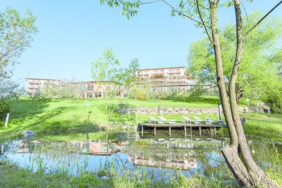 Retter Bio Natur Resort - Photo prise en contre bas devant la piscine naturelle et au dessus on voit les bâtiments de l'hotel derrière les arbres