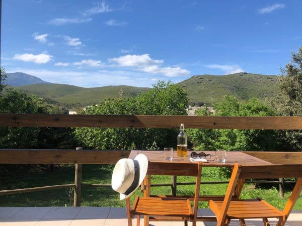 Terrasse ensoleillée face aux montagnes avec une table et des chaises en bois.