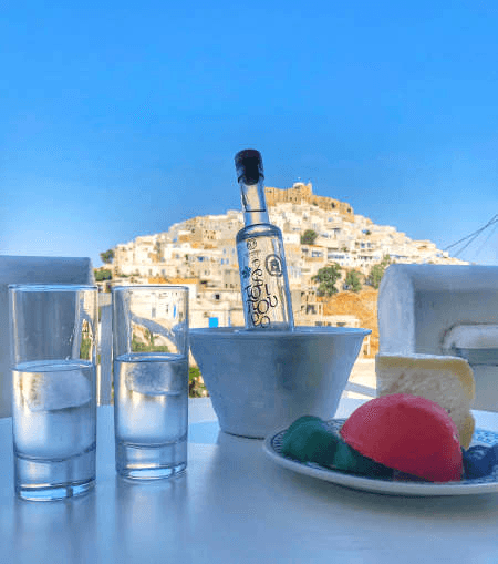 sur une table de la terrasse avec vue une bouteille de ouzo, 2 verres et du fromage de brebis