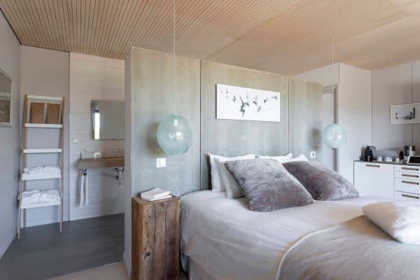 Intérieur de la chambre dans les tons blanc et gris avec en tête de lit un mur en beton brut qui cache la salle de bain