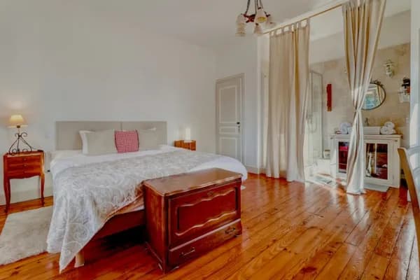 Chambre double avec un dessus de lit où est brodé le nom Arthur Rimbaud, à la gauche du lit une armoire blanche avec son portrait dessus et à droite un bureau en bois et sa chaise noire