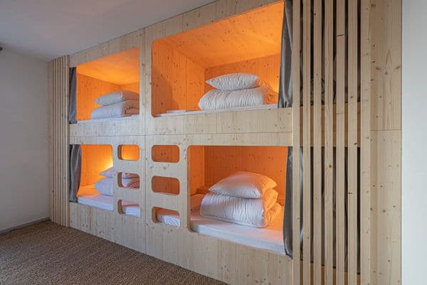 Dortoir de 4 personnes avec 2 lits superposés en bois et chacun un rideau gris