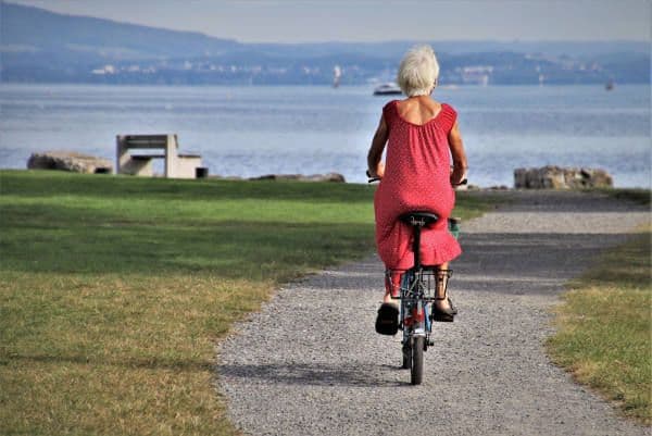 Femme avec une robe rouge de dos sur un vélo se dirigeant vers la mer