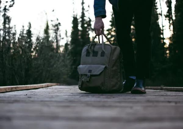 Un homme pose son sac à dos voyage par terre. Derrière lui une forêt de pins