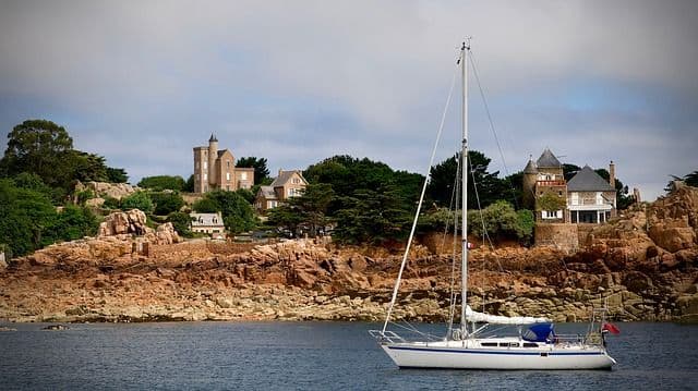 écotourisme en bretagne - Un voilier voiles rangées devant la côte rocheuse en Bretagne