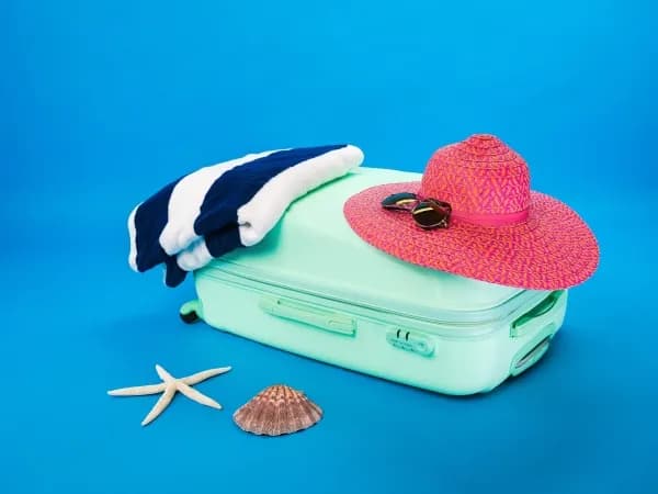 serviette bleue et blanche placée à côté d'un chapeau rose tous les deux posés sur une petite valise 