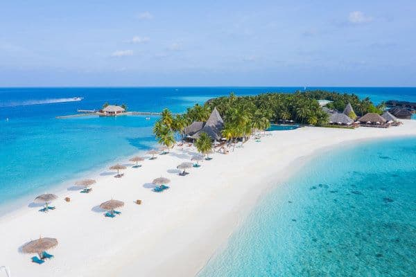 Photo vue du ciel de l'ile on y voit l'hotel protégé et entouré de palmiers, des transats sous des parasols sur une plage de sable blanc et la mer émeraude qui entoure l'ile